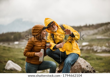Middle age couple with backpack taking break of hiking in a beautiful nature and taking tea or water from a thermos flask