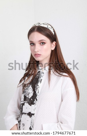 Close up vertical fashion portrait of a teenage female model with professional make up and trendy hair band accssory, wearing white cotton dress and posing in studio
