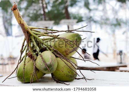 The coconut is placed on a white table with a beach backdrop.