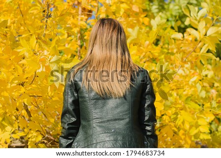 Portrait of a young blonde of European descent in a black jacket, against a background of yellow leaves. Young woman in the autumn forest.Photo taken in October