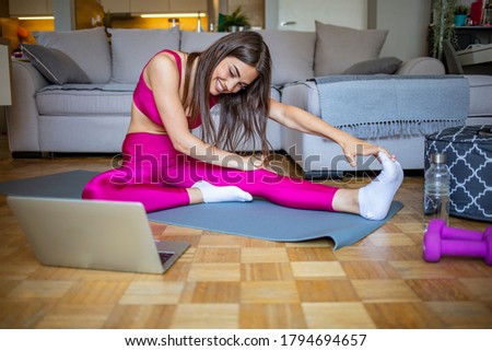 Young woman exercising at home in a living room. Video lesson. Young woman repeating exercises while watching online workout session. Beautiful young woman doing fitness exercise at home