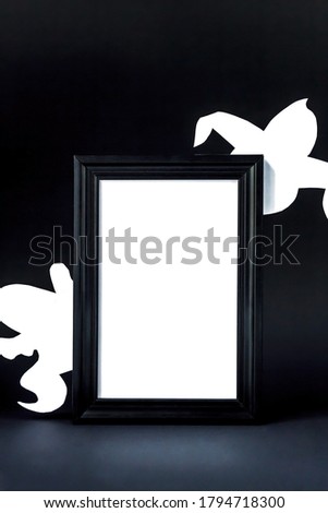 Background for Halloween. Black frame with free space on a black background. White ghostly figures peek out from behind an empty black photo frame.  