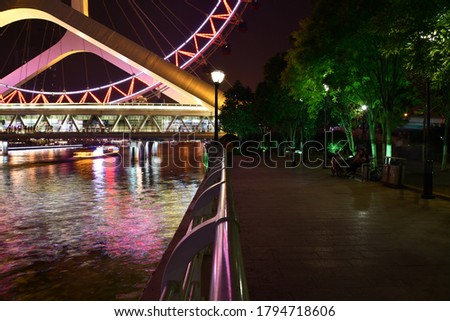 the way or riverside walk towards the ferry's wheel at night Tianjin Eye at night with some green trees and bushes