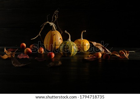 Background for writing text. 3 decorative pumpkins, a few small red apples and dry autumn leaves are on the dark wood background. Halloween decoration , traditional holiday. Hard sunny side ligh