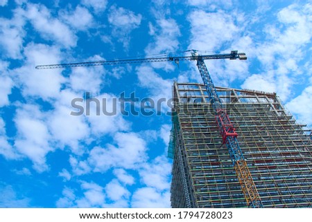 Construction crane lifting load during construction of multi-storey building. Construction of skyscraper against blue sky. Apartment building. Modern architecture. Stylish living block of flats
