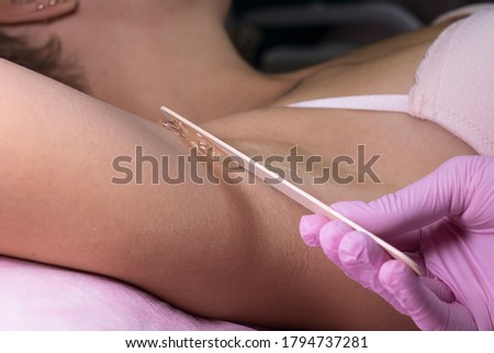 
A beautician applies a disposable wooden stick epilation gel to the armpits
