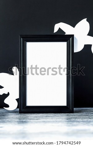 Background for Halloween. Black frame with free space on a table with a black background. White ghostly figures peek out from behind an empty black photo frame. Halloween typography concept and ideas.
