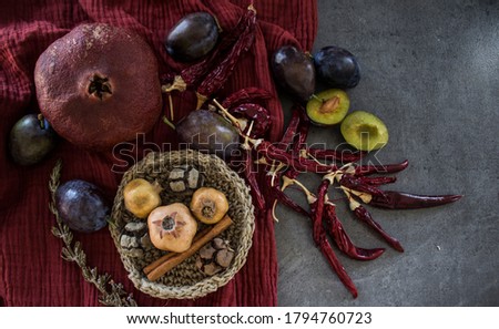 Still life with dried pomegranate and red chili peppers. Red textured drapery on background. Autumn mood picture.  