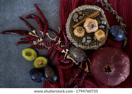 Still life with dried pomegranate and red chili peppers. Red textured drapery on background. Autumn mood picture.  