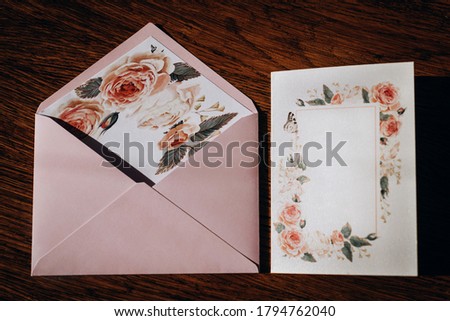 
On a wooden table lies a wedding invitation drawn with watercolor paints of the bride and groom and a pink envelope.