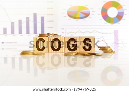 Cost of goods sold. COGS the word on wooden cubes, cubes stand on a reflective surface, in the background is a business diagram. Business and finance concept