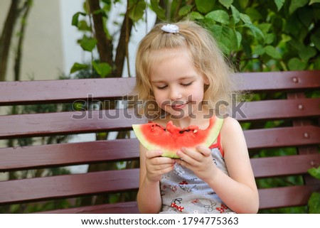 Funny cute blond girl eating watermelon outdoors in summer park.  Child, baby, healthy food.