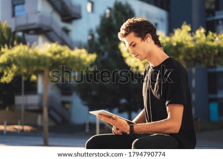 Handsome young man studying online on digital tablet while sitting at college campus. High quality photo