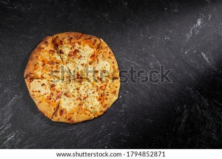 Sliced Pizza on black stone background, top view. Ultimate Four Cheese Pizza with Cheddar Mozzarella Ricotta Parmesan Cheese