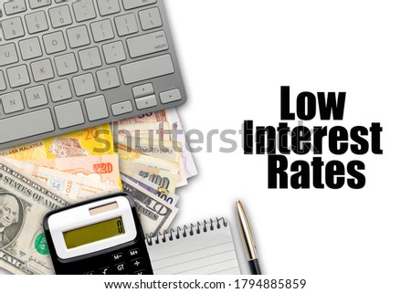 LOW INTEREST RATES text with fountain pen, keyboard, calculator, notepad and currency banknotes on white background. Business Concept