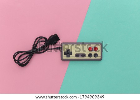 Wired retro gamepad (joystick) with wound cable on pink blue background. Video game, gaming. Top view