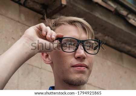 Portrait of a young man straightening his glasses. Handsome young man with fashionable hairstyle looks into the distance. Lifestyle.