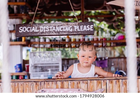 Little baby boy on vacation in thailand with social distance sign at bar.
