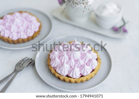 Marshmallow mini cake - berry tart or tartlet with pink cream on top. Beautiful dessert on plate, white table with flowers. Selective focus with copy space.