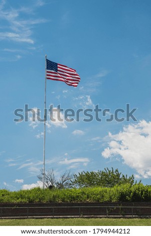 A vertical shot of an American flag waving on a pole with a blue sky background