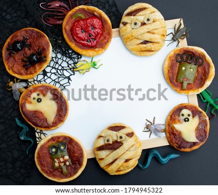 Halloween mini pizza with cheese, olives and ketchup.  Decorated mummy, ghost, spiders, pumpkin.  On a black background. FlatLay. Top view. Plase for text