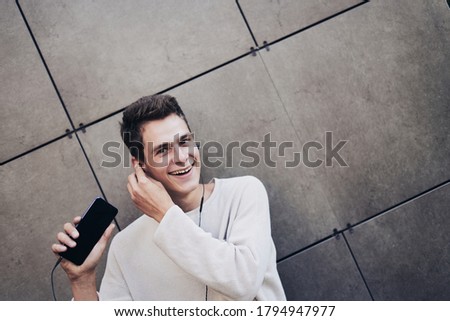 Young guy standing on street listening to music with smartphone