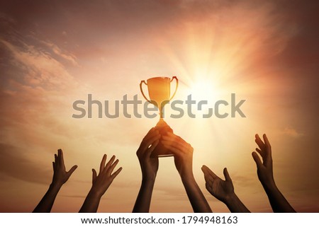 Winning team with gold trophy cup against shining sun in sky  Royalty-Free Stock Photo #1794948163