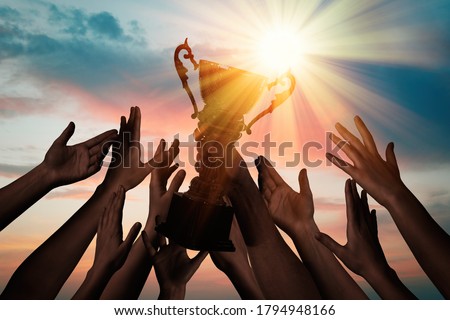 Winning team with gold trophy cup against shining sun in sky  Royalty-Free Stock Photo #1794948166