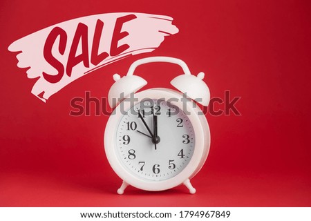 White round plastic alarm clock on a red background and the inscription Sale. Black Friday concept, sale season, copy space. Template, layout for your design.