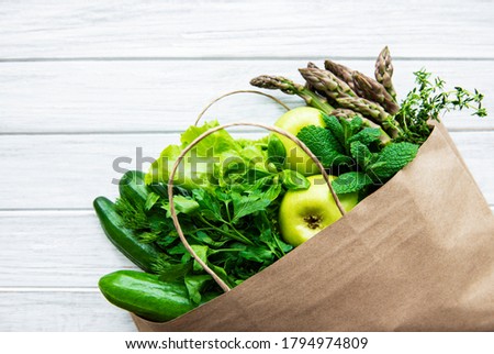 Top view of green vegetables in shopping bag on white wooden table
