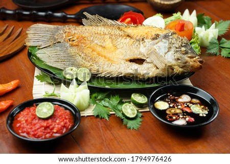 photos of food products, Close up of fried fish or fried gouramy with chili sauce and vegetables on a textured wooden table. Usually used for menu list pictures or food pictures in restaurant. top view