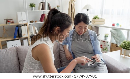 beautiful lady showing ultrasound photo to sister in sofa.