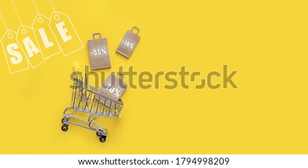 Metal shopping basket with paper bags, discounts, sale label on a yellow background. The view from the top, flat lay. The concept of shopping in stores and online, sales and black Friday.