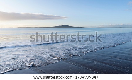 Milford beach at sunrise with swirl waves in the foreground and Rangitoto Island in the distance