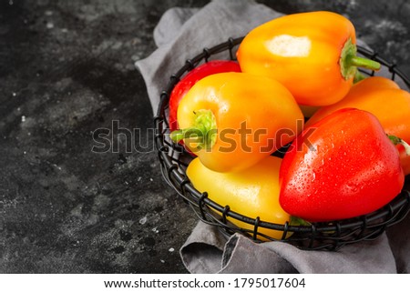 Red, yellow and orange peppers in a basket on the black kitchen table. Paprika close up