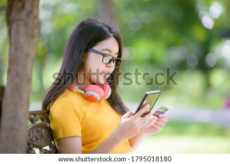 Asian young woman with a credit card is relaxing an order online in the garden.