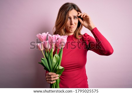 Young beautiful brunette woman holding bouquet of pink tulips over isolated background worried and stressed about a problem with hand on forehead, nervous and anxious for crisis