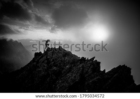 Sport photo in mountains. Silhouette of runner on the top of the hill, sunset sky in background. Black and white
