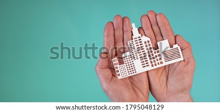 Concept of business insurance with paper building in hands on turquoise color background Royalty-Free Stock Photo #1795048129