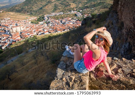 Stock photo of a rear view of a woman contemplating the landscape of a village surrounded by nature in a valley. Beautiful woman sitting on a grindstone contemplating a beautiful landscape. Travels