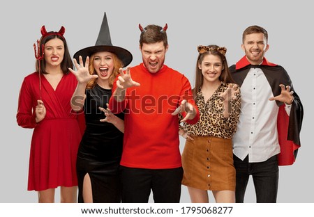 friendship, holiday and people concept - group of happy smiling friends in halloween costumes of vampire, devil, witch and leopard scaring over grey background