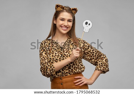 holiday, photo booth and people concept - happy smiling woman in halloween costume of leopard with ears and scull party accessory over grey background