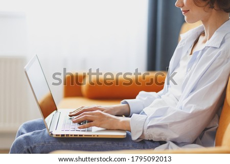 Cropped image of young woman in casual clothes sitting on couch spending time in living room at home. Rest relax good mood leisure lifestyle concept. Mock up copy space. Working on laptop pc computer