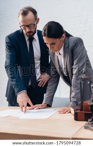 selective focus of bearded lawyer pointing with finger at document near businesswoman in office