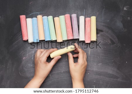multicolored chalk on a black background and two female hands, top view
