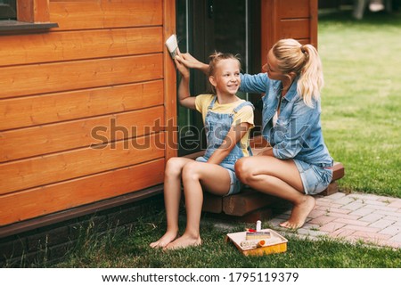 Mom teaches daughter to paint a house on the street with a brush. A happy family. Home Improvement, DIY Repair.