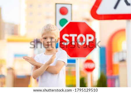 a child stands at a STOP sign and holds his hands in a cross, traffic rules for children