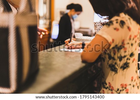 Woman client signing hotel contract paper at reception desk In face mask