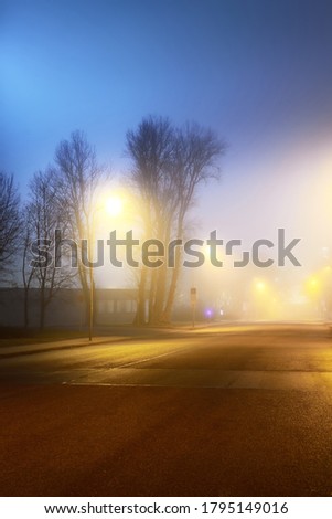 An empty illuminated motorway and closed shops in a fog at night. Road sign close-up. Dark urban scene, cityscape. Riga, Latvia. Dangerous driving, concept image