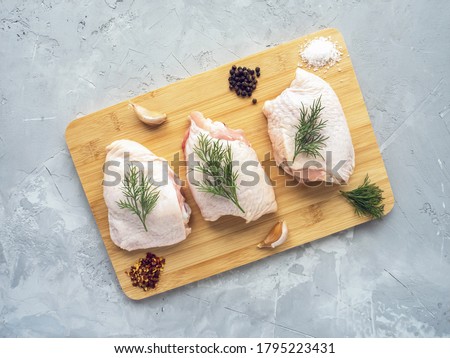 Raw chicken thighs on cutting board with ingredients for cooking at grey concrete kitchen table. Top view with copy space. Royalty-Free Stock Photo #1795223431